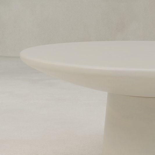 A close-up of the Arrio Table, a modern circular design in light beige with a thick, broad base, set against a matching neutral-toned background.