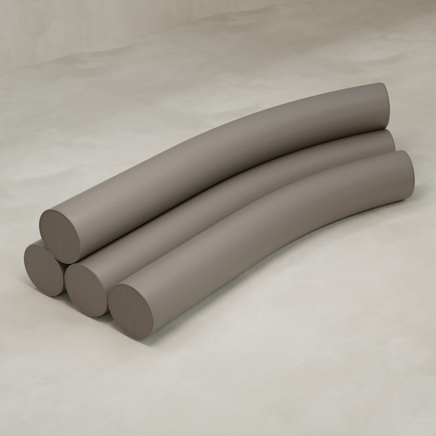 Four large, smooth, taupe cylinders are stacked on a light textured surface. The top two curve gently, forming the arching silhouette of the Cylindra Sofa over the two below.