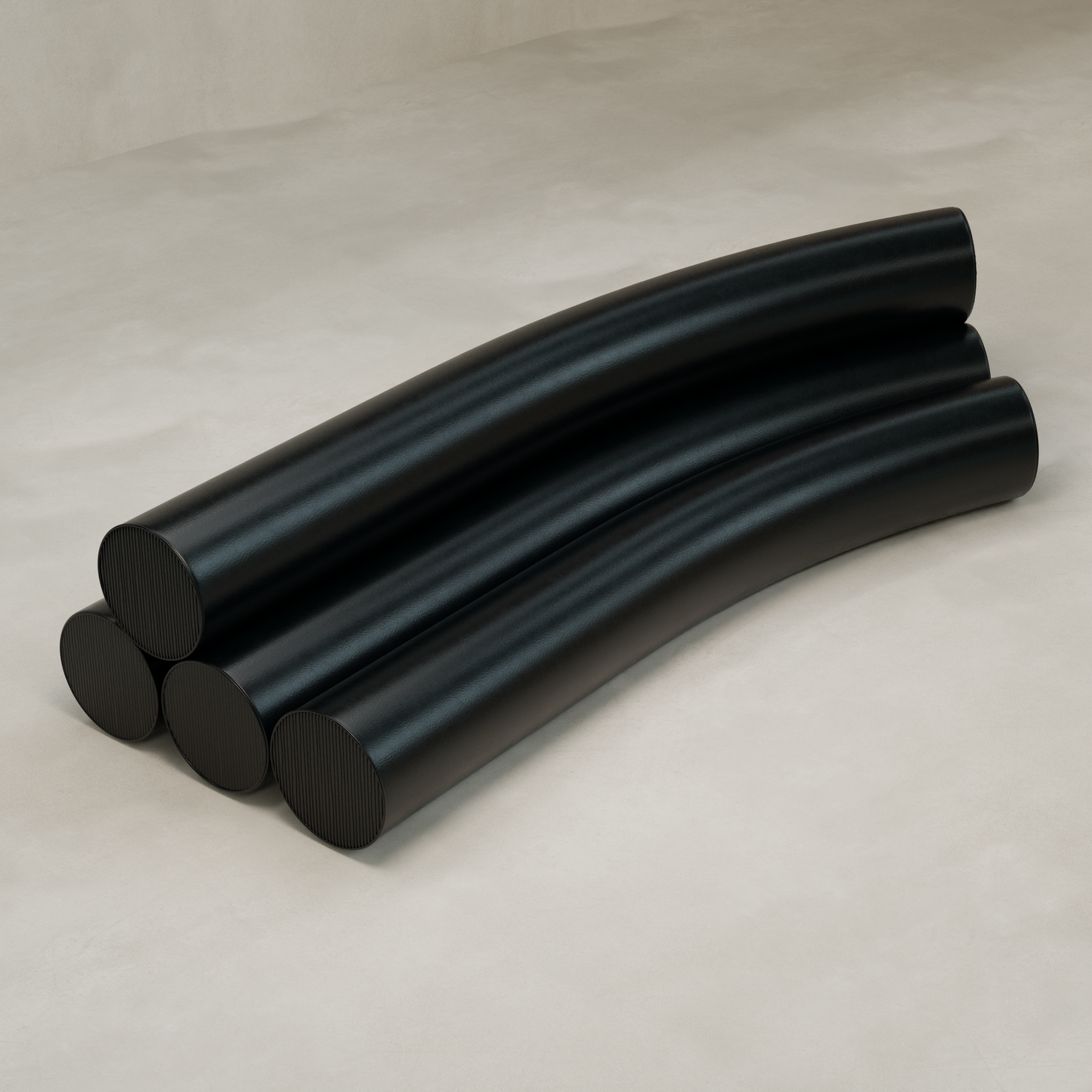 Four large, smooth, black Cylindra Sofa pieces are stacked in two layers on a light beige surface. Slightly curved and neatly arranged, they resemble a modern sofa or minimalist industrial sculptures.