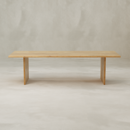The Elm Farmhouse Table is a simple rectangular dining table made from aged Elm, with clean lines and two wide flat legs, shown against a light neutral background.