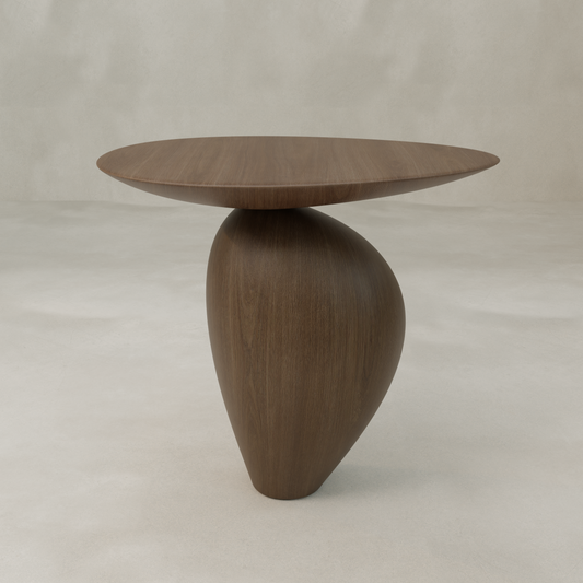 The Noyer Side Table features a modern wooden design with an oval top and a unique asymmetrical curved base, adding sculptural style against a neutral, light background.