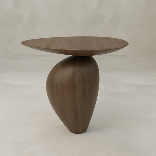 The Noyer Side Table features a modern wooden design with an oval top and an asymmetrical curved base, showcasing sculptural furniture against a plain, light background.
