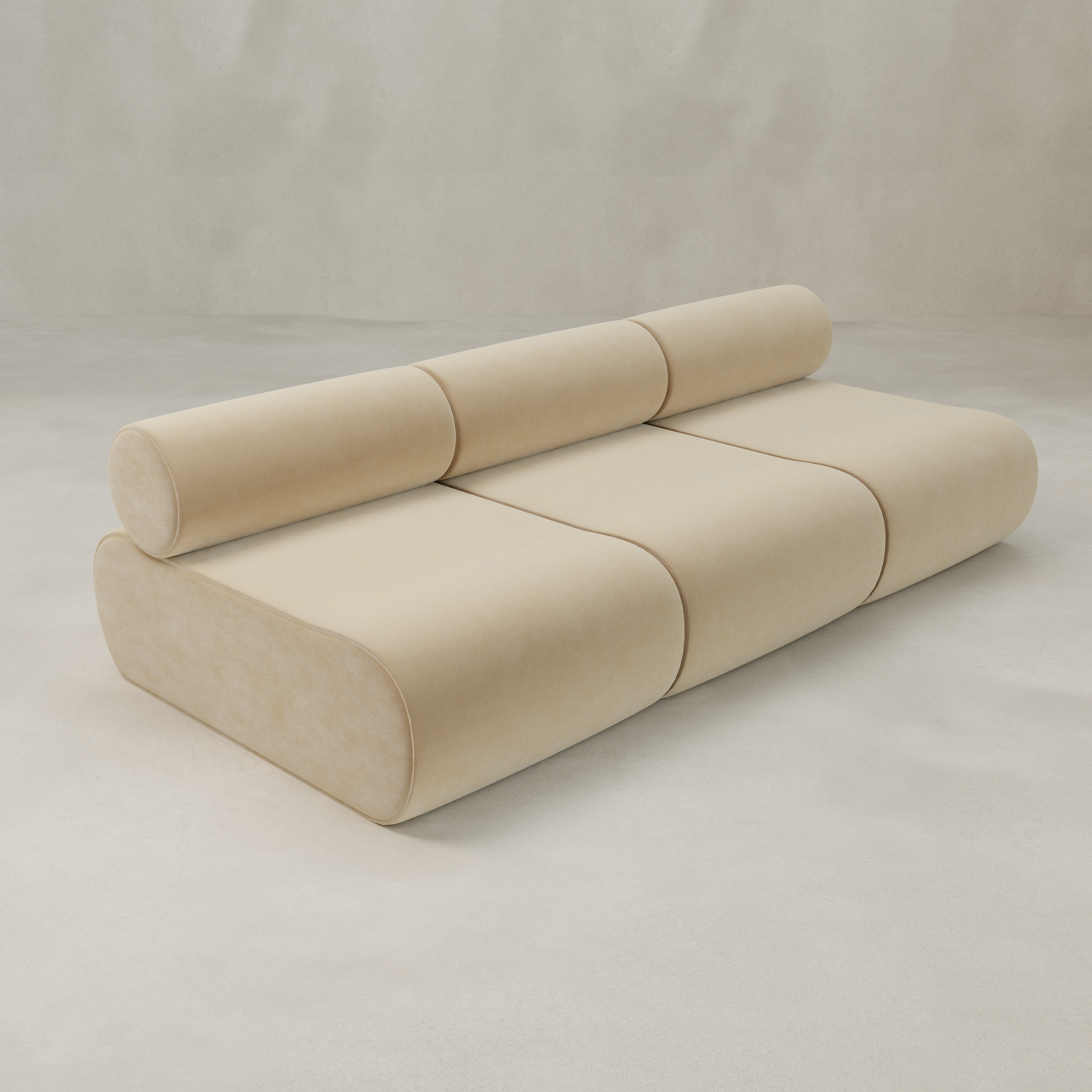 The Nuage Three Seater Modular Sofa in beige velvet features a modern, minimalist design with a cylindrical backrest and rounded edges, displayed against a light, neutral background.