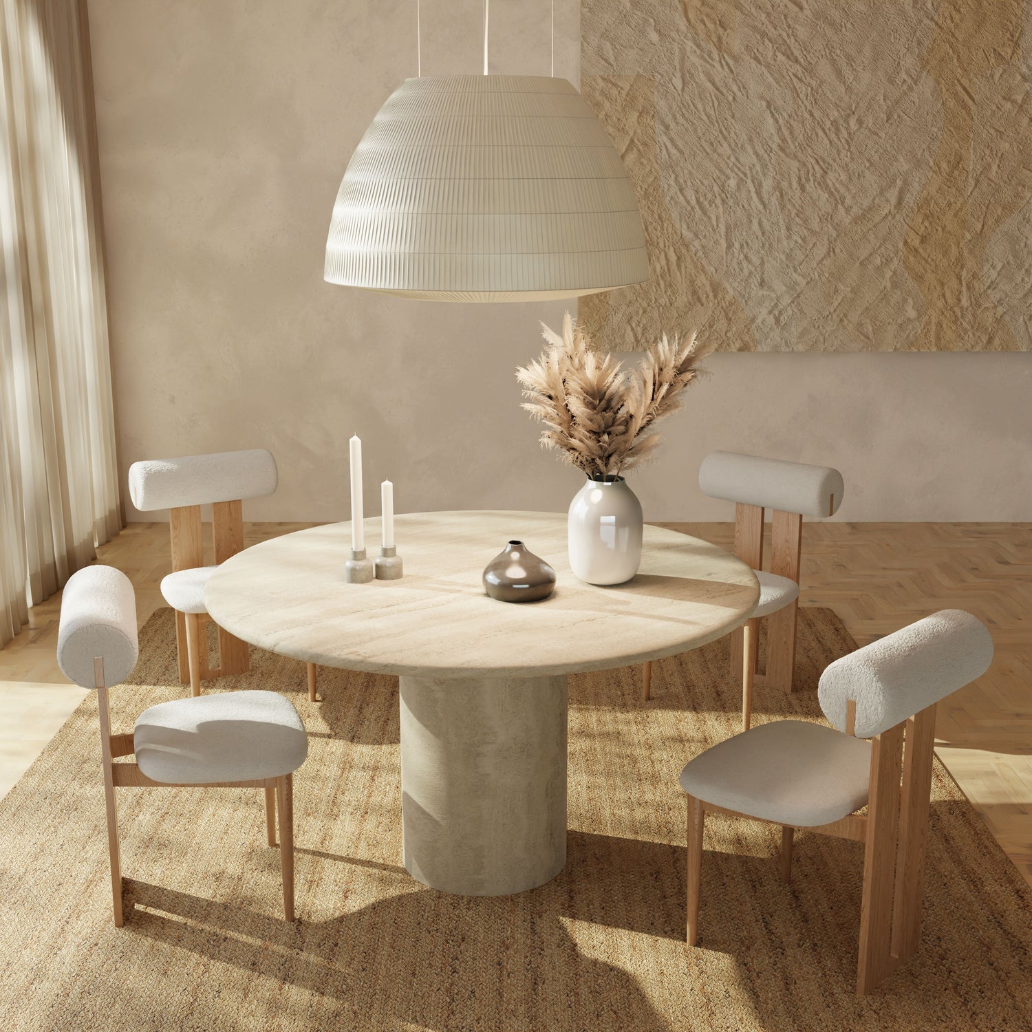A minimalist dining room featuring the Renè + Templeton Dining Set—a round travertine pedestal table with four bouclé chairs—plus a large pendant lamp, candles, and a ceramic vase with pampas grass. Sunlight from the left highlights the neutral decor.