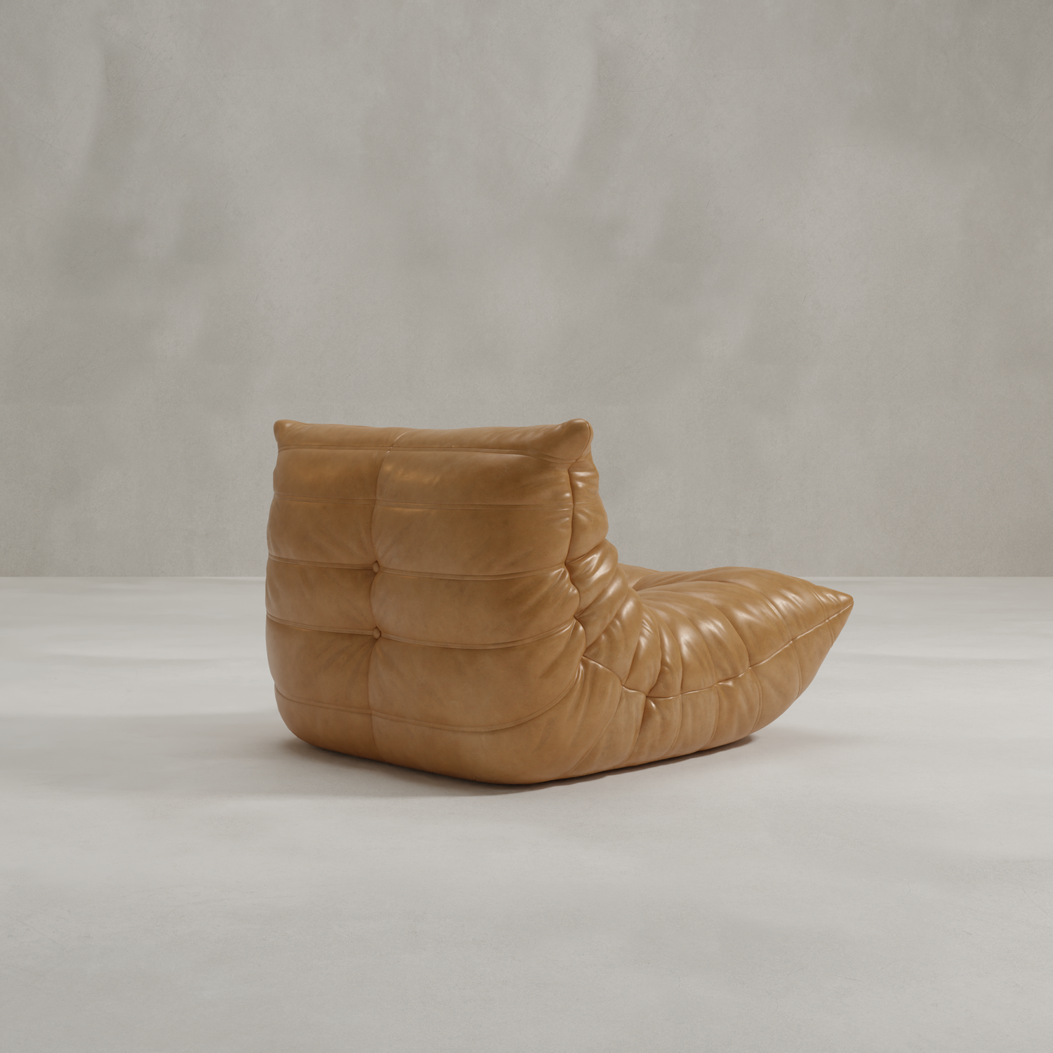 The Rolo Lounge Chair, a modern tan leather piece with a low seat and quilted, tufted cushioning inspired by mid-century design, sits on a light gray floor against a textured light gray wall.