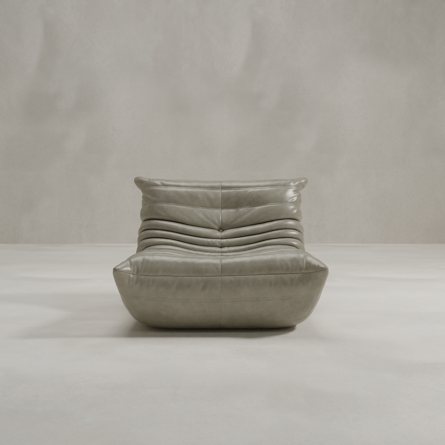 The Rolo Lounge Chair features a modern, low-profile design with gray leather upholstery and plush segmented detailing, evoking subtle 70s lounge vibes in a minimal setting with smooth, light gray walls and floors.
