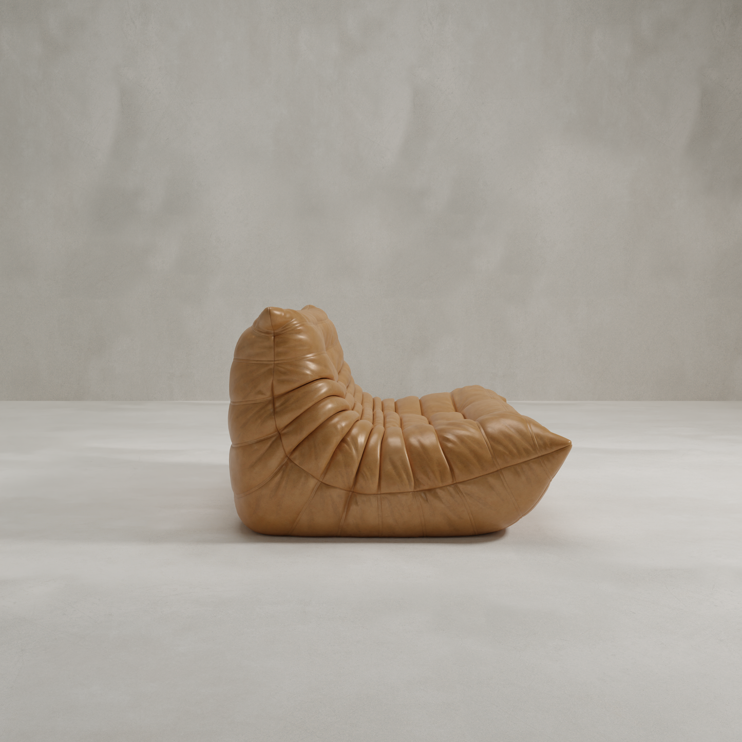 The Rolo Lounge Loveseat, a low armless tan leather seat with deep tufting and a modern sculpted 70s-inspired shape, sits on a light concrete floor against a plain textured gray wall.