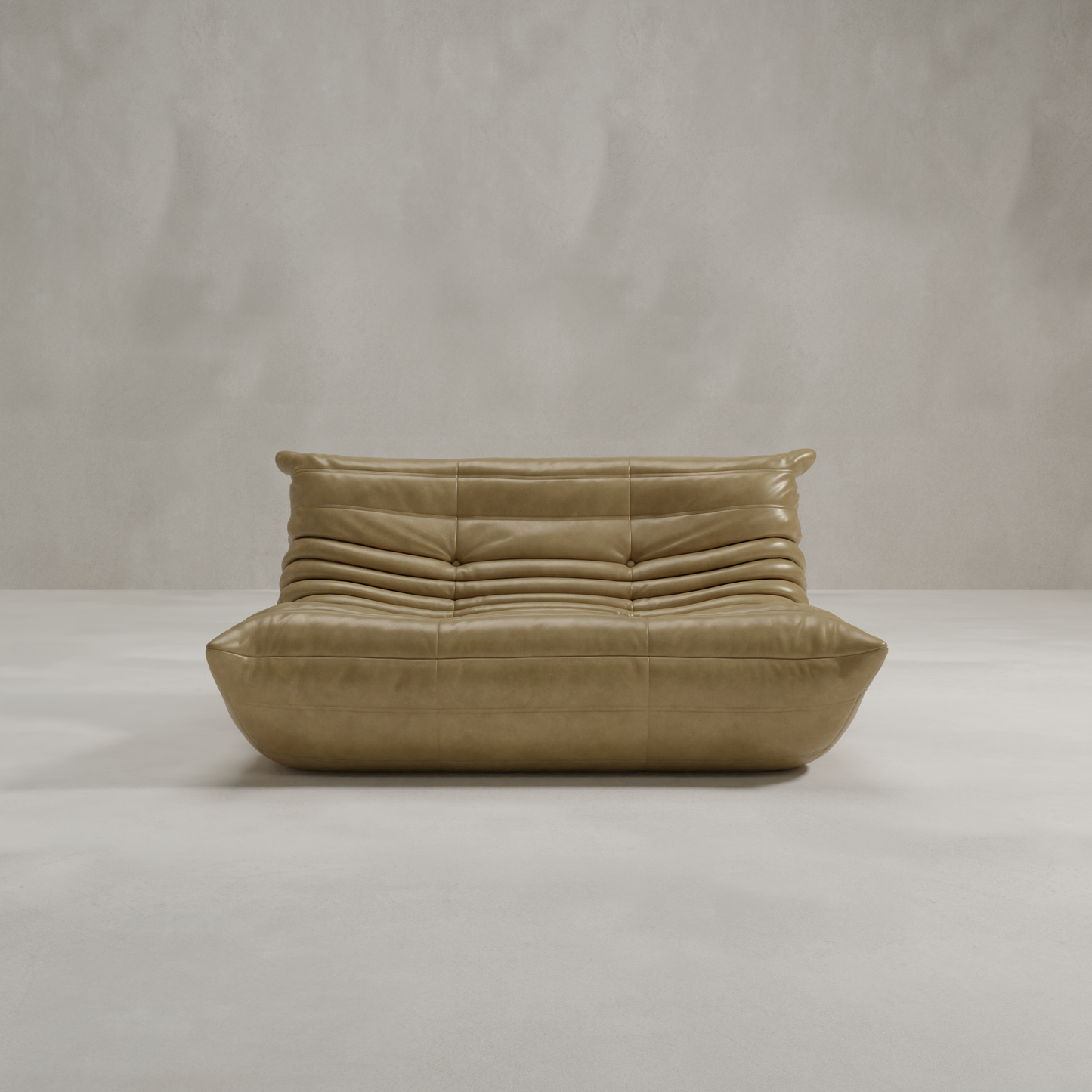 The Rolo Lounge Loveseat, a modern low-profile tan leather seat with plush horizontally-stitched cushions, is placed in a minimal light-gray room with mid-century design elements and a smooth concrete floor against a textured wall.