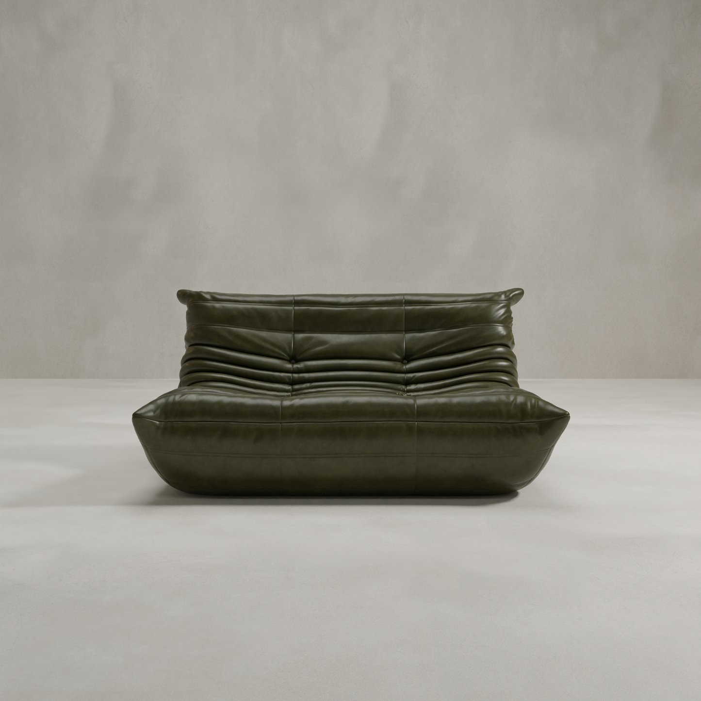 The Rolo Lounge Loveseat, a modern dark green leather piece with ruched cushions and a low profile inspired by mid-century design, is placed in a minimalist room featuring light gray walls and flooring.