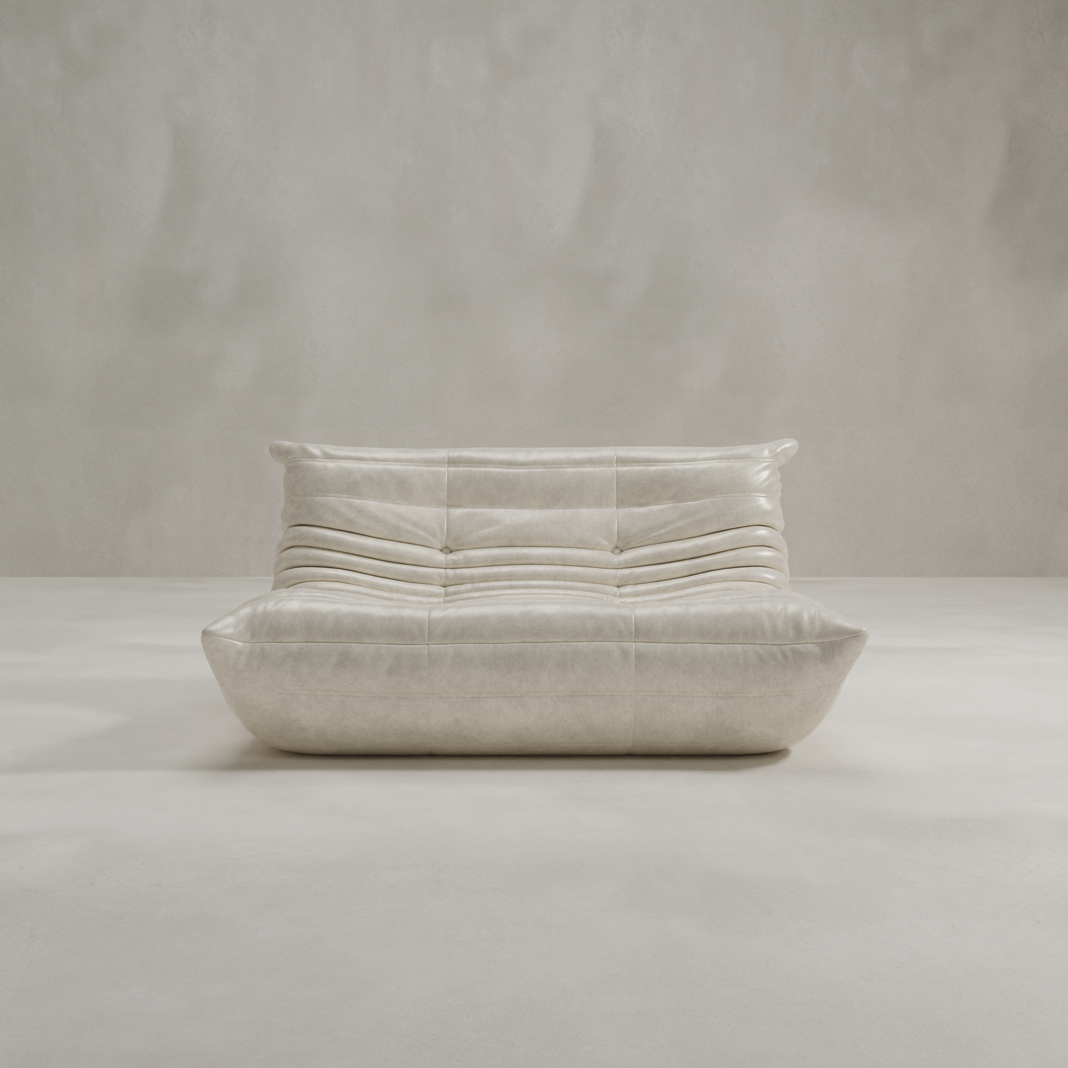 The Rolo Lounge Loveseat, a modern cream leather sofa with a low profile and gently curved quilted cushions inspired by mid-century design, is centered in a minimal light gray room with smooth floors and plain textured walls.