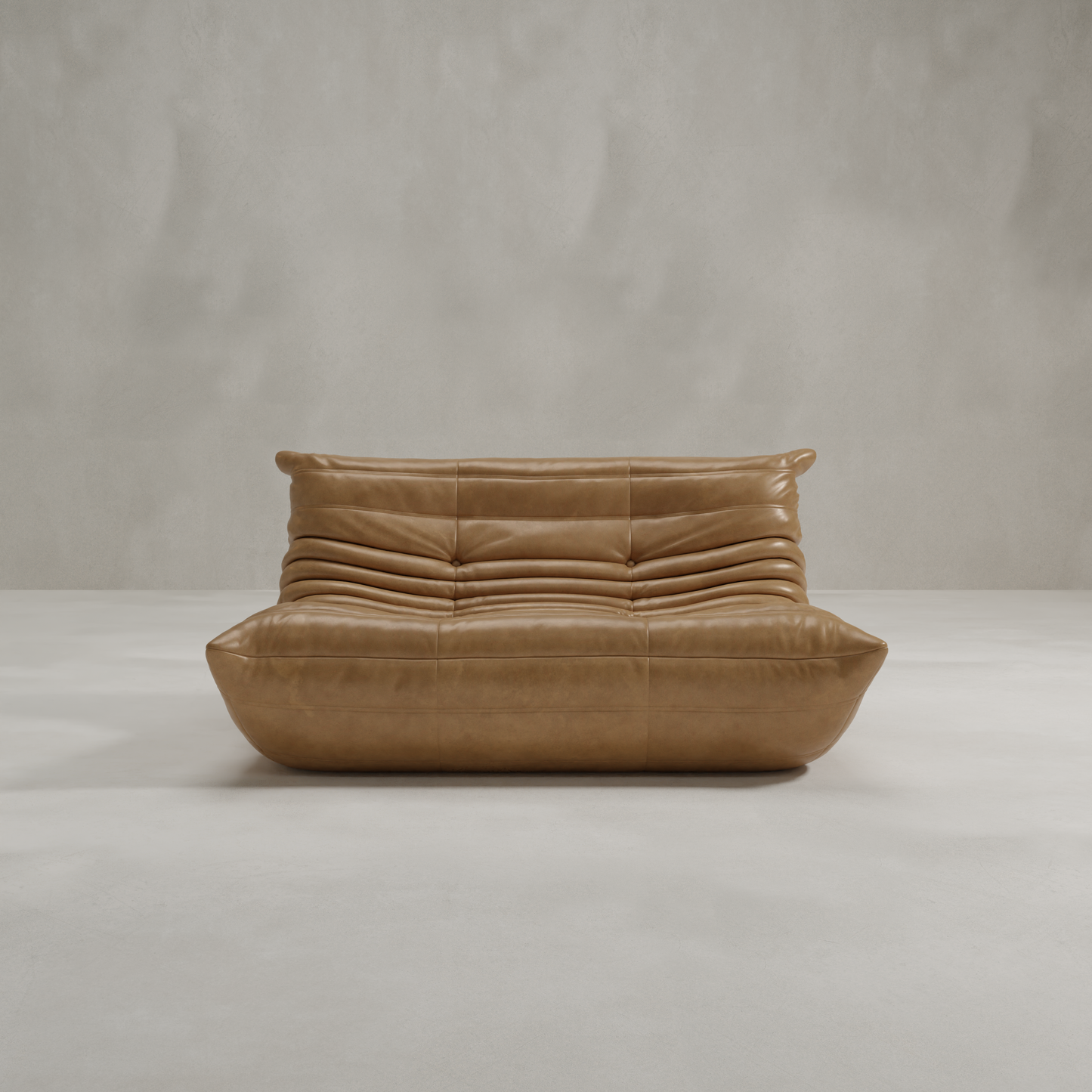 The Rolo Lounge Loveseat is a modern tan leather sofa with a low profile, rounded edges, and horizontal tufting that channels mid-century design, set against a plain light gray wall and floor.