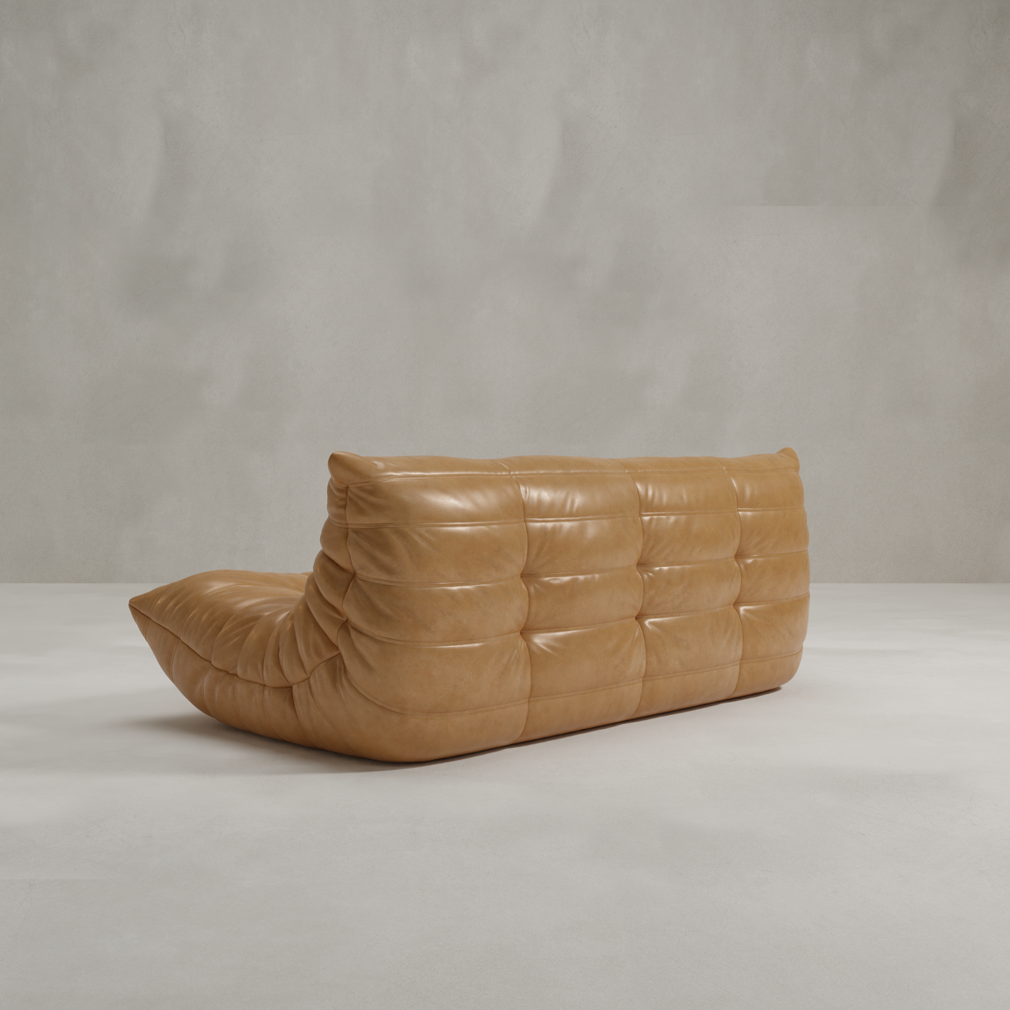 The Rolo Lounge Three Seater is a modern tan leather sofa with tufted, curved shapes inspired by mid-century design, shown here against a plain light gray textured wall and floor.