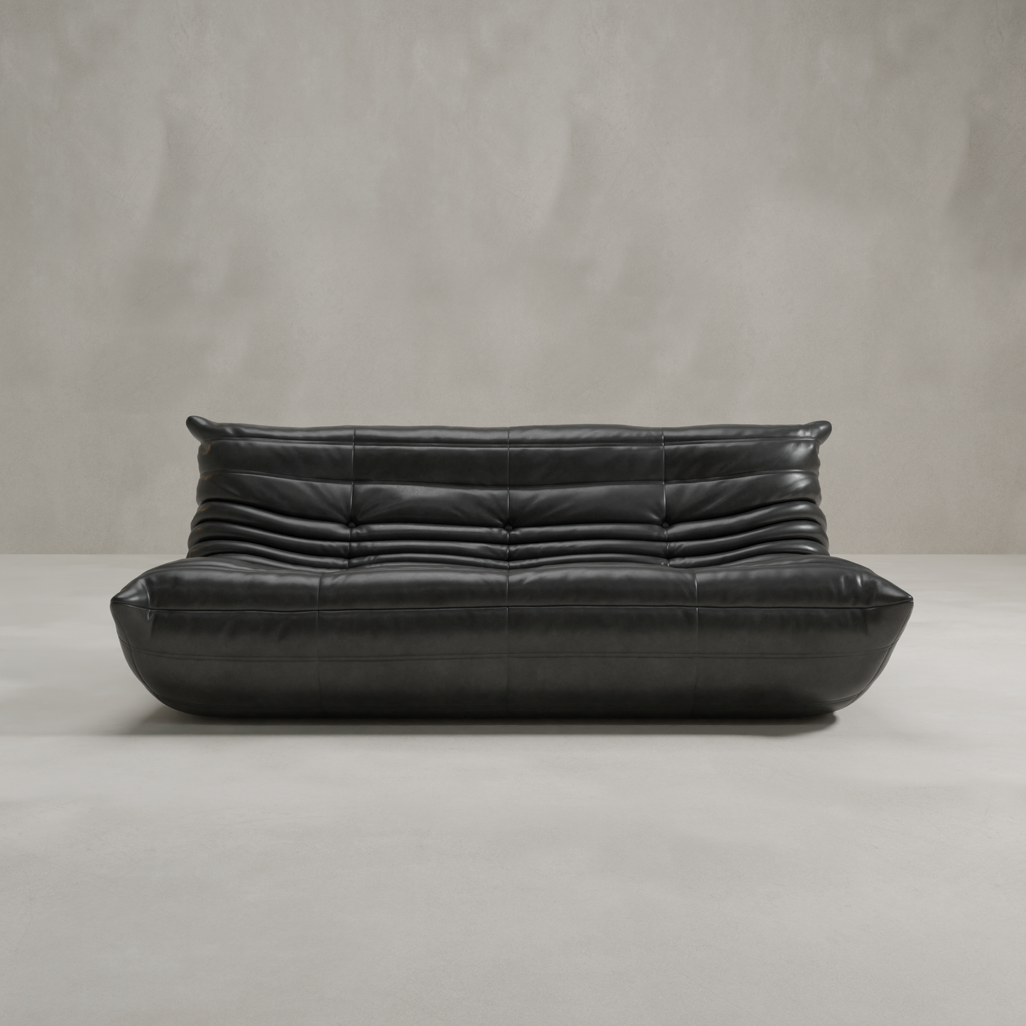 The Rolo Lounge Three Seater is a modern black leather sofa with deep horizontal tufting and a low, rounded design, evoking mid-century style as it rests on a light gray floor against a smooth beige wall.