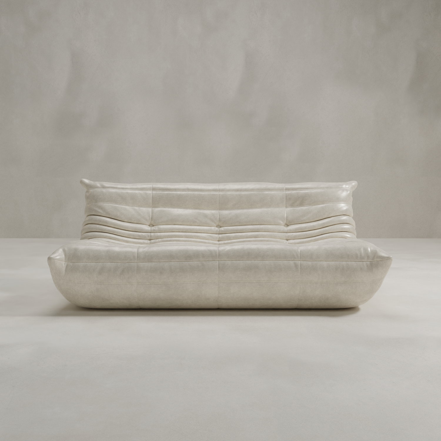 The Rolo Lounge Three Seater is a modern, low-profile beige leather sofa with tufted cushions and curved lines, set against a neutral wall and floor for a timeless mid-century look.