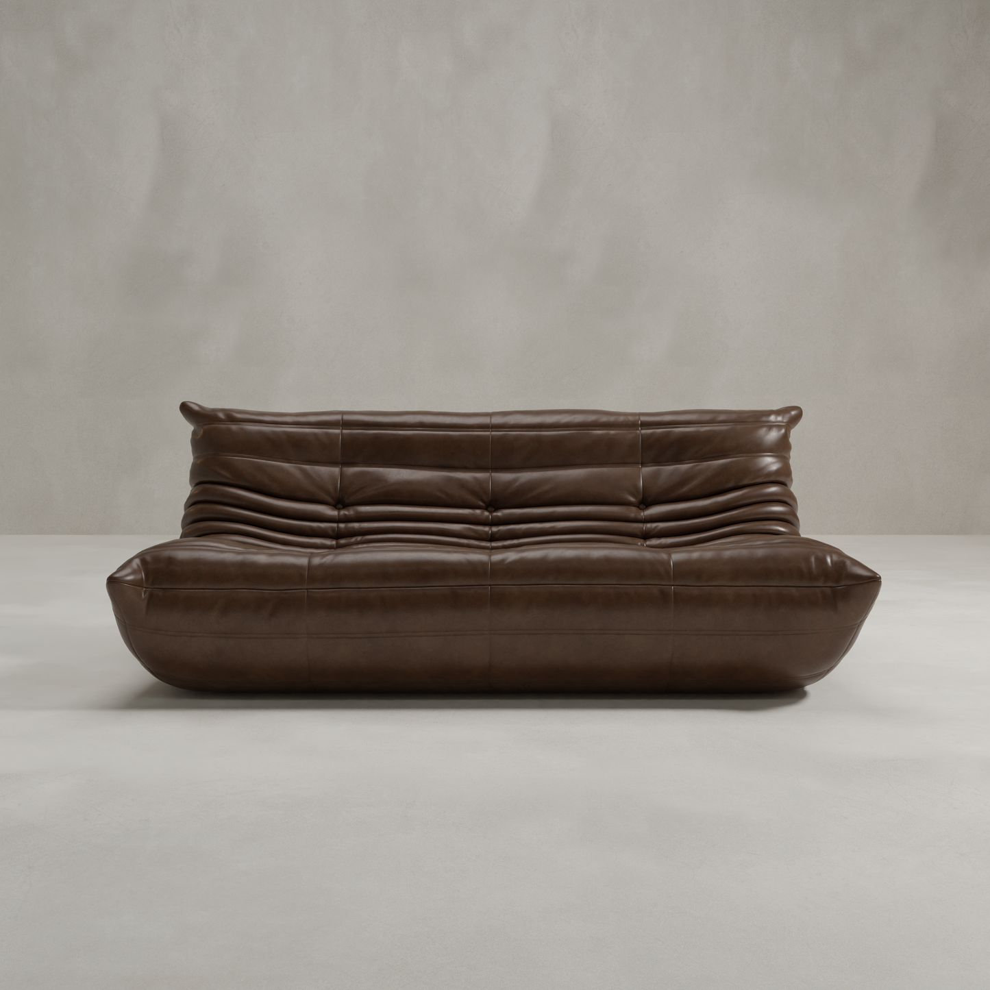 The Rolo Lounge Three Seater is a modern brown leather sofa with a low profile and tufted seat and backrest, highlighting mid-century design. It sits on a smooth light-colored floor against a plain gray wall.