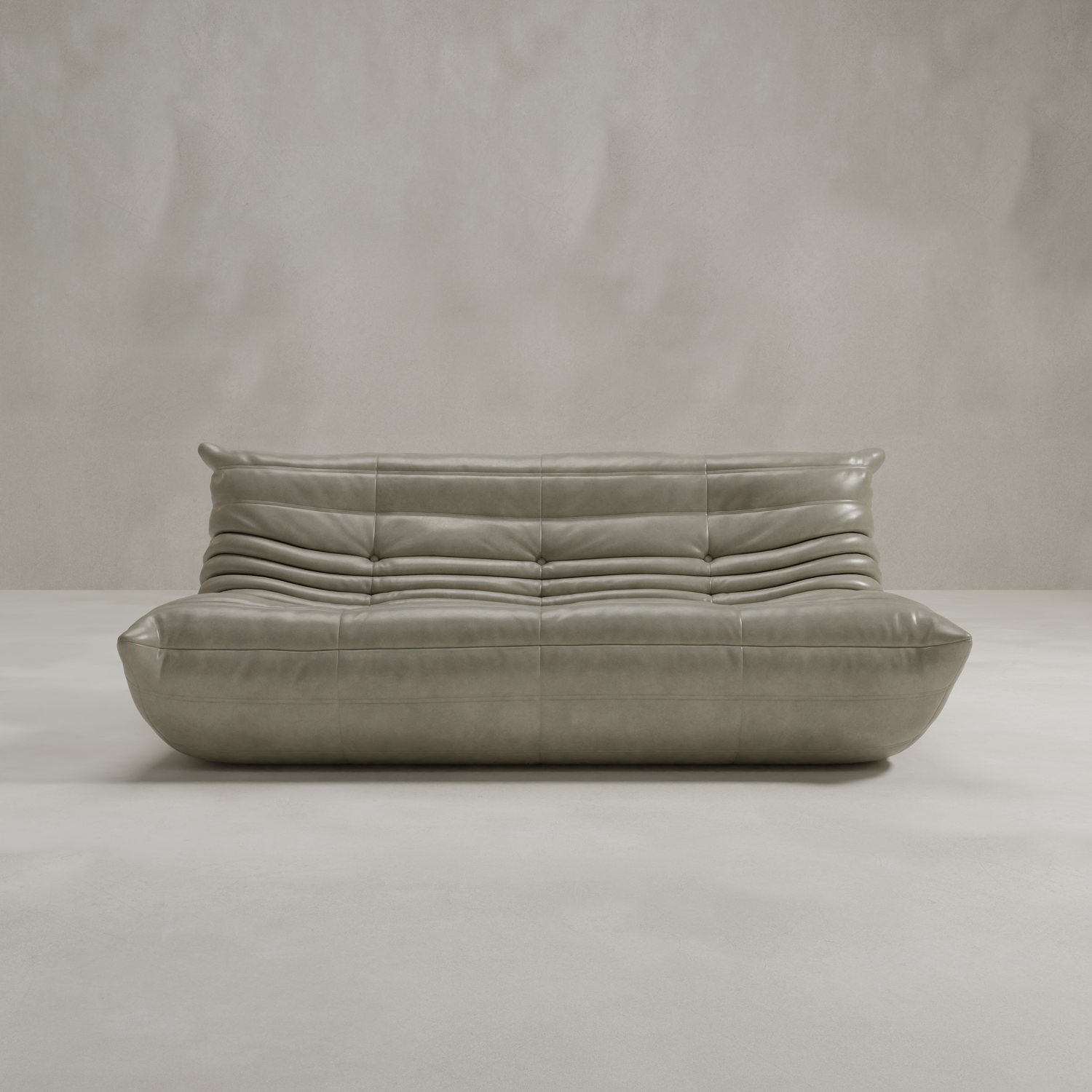 The Rolo Lounge Three Seater is a modern, low-profile gray leather sofa with tufted cushions and minimalist, mid-century-inspired design, shown against a plain light background.