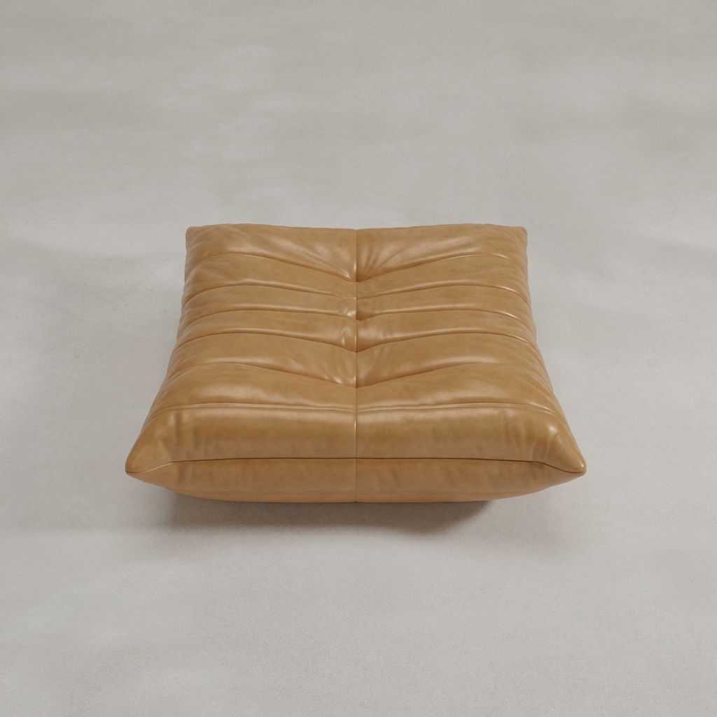 The Rolo Ottoman is a large, square tan leather floor cushion with soft horizontal tufted seams, perfect as a versatile ottoman or extra seating, shown here on a light gray surface.