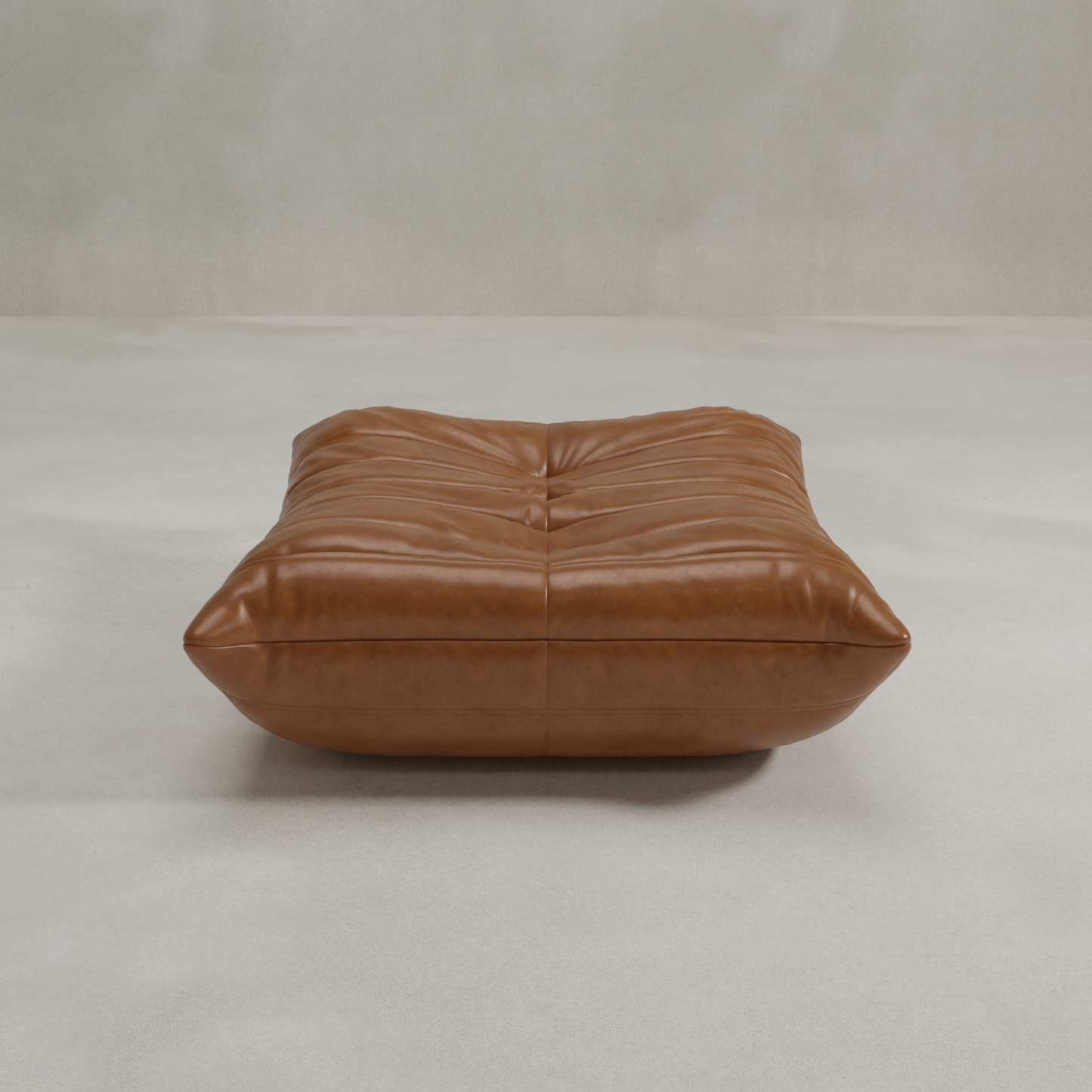 The Rolo Ottoman is a large, rectangular, tufted brown leather floor cushion that serves as a versatile ottoman, shown on a light grey surface in front of a plain grey wall.