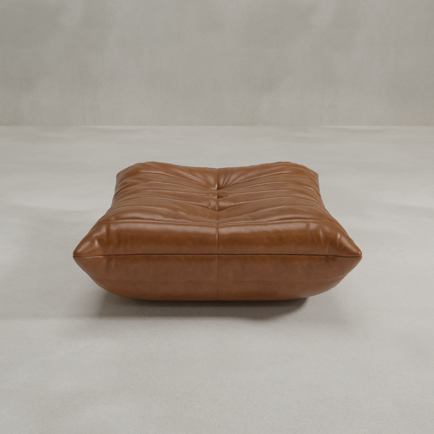 The Rolo Ottoman is a large, rectangular, tufted brown leather floor cushion that serves as a versatile ottoman, shown on a light grey surface in front of a plain grey wall.
