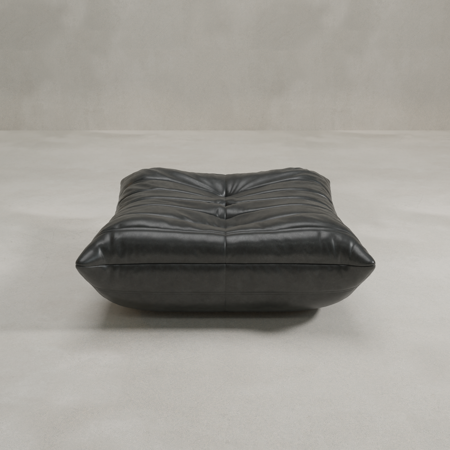 The Rolo Ottoman, a low black leather piece with a tufted cushioned top, sits on a light gray floor against a plain, textured wall.