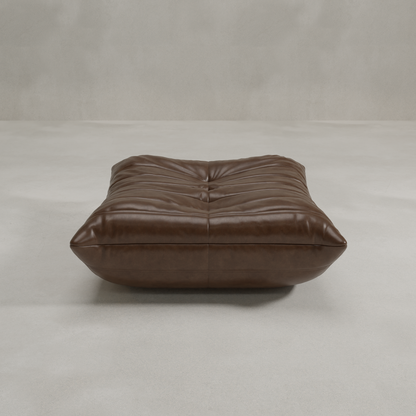 The Rolo Ottoman, a low rectangular pouf with soft brown leather tufted upholstery, offers versatile use as extra seating or a footrest. It rests on a light gray floor against a plain, textured wall.