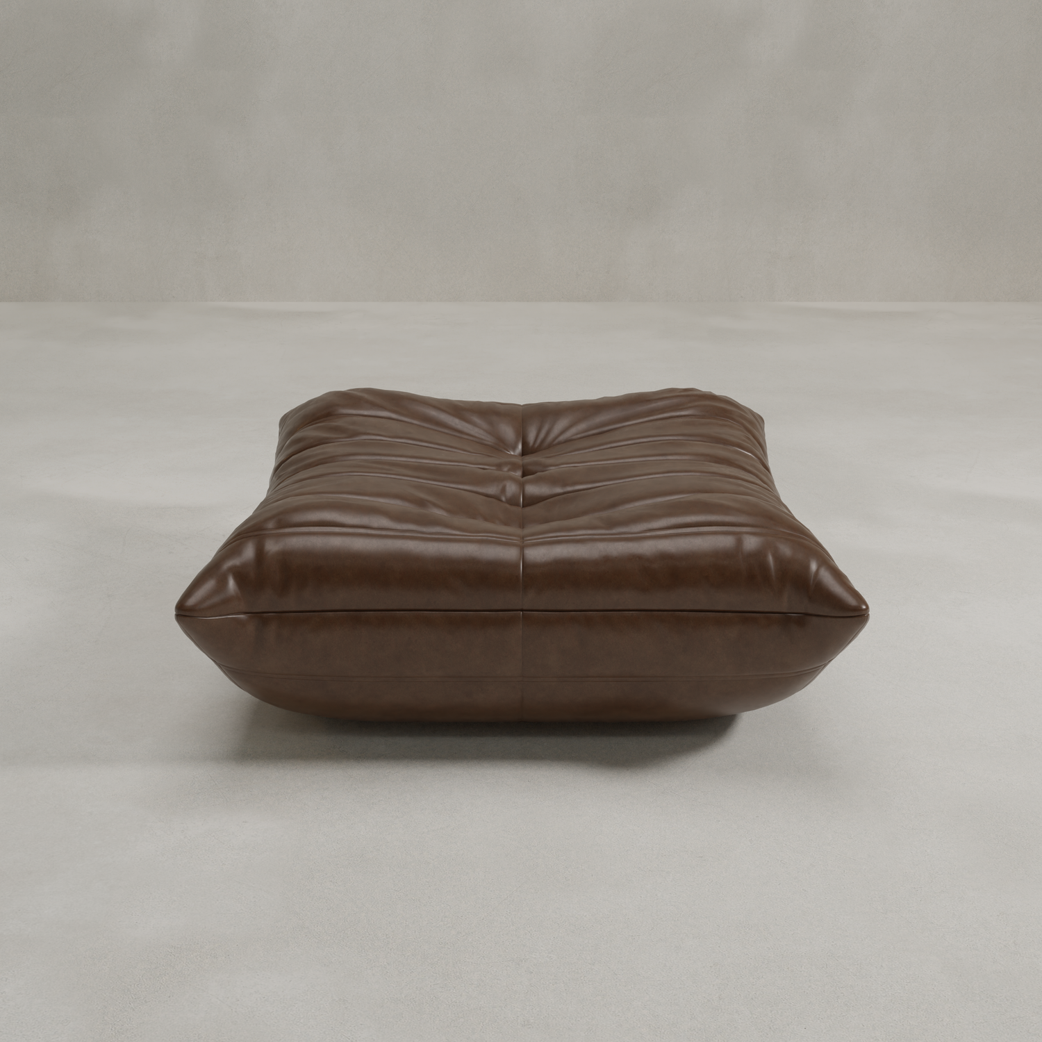 The Rolo Ottoman, a low rectangular pouf with soft brown leather tufted upholstery, offers versatile use as extra seating or a footrest. It rests on a light gray floor against a plain, textured wall.