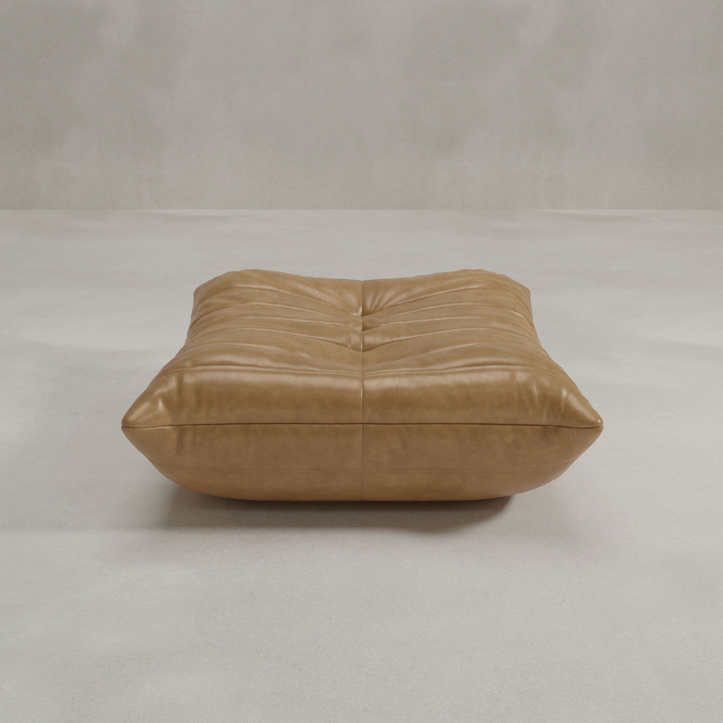 The Rolo Ottoman is a large tan leather floor cushion with tufted details and a soft, padded look, ideal as an ottoman or extra seat. It rests on a smooth light gray surface with a plain, light background.