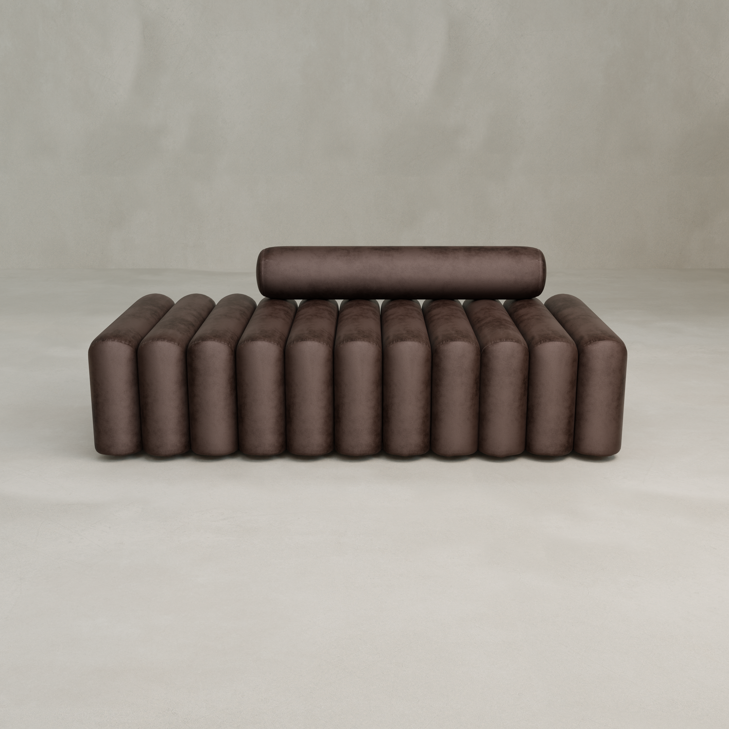 The Sonorra Bench Large is a modern, minimalist brown bench with quilted velvet upholstery, a cylindrical backrest with vertical padded sections, set on a light floor against a plain gray wall.
