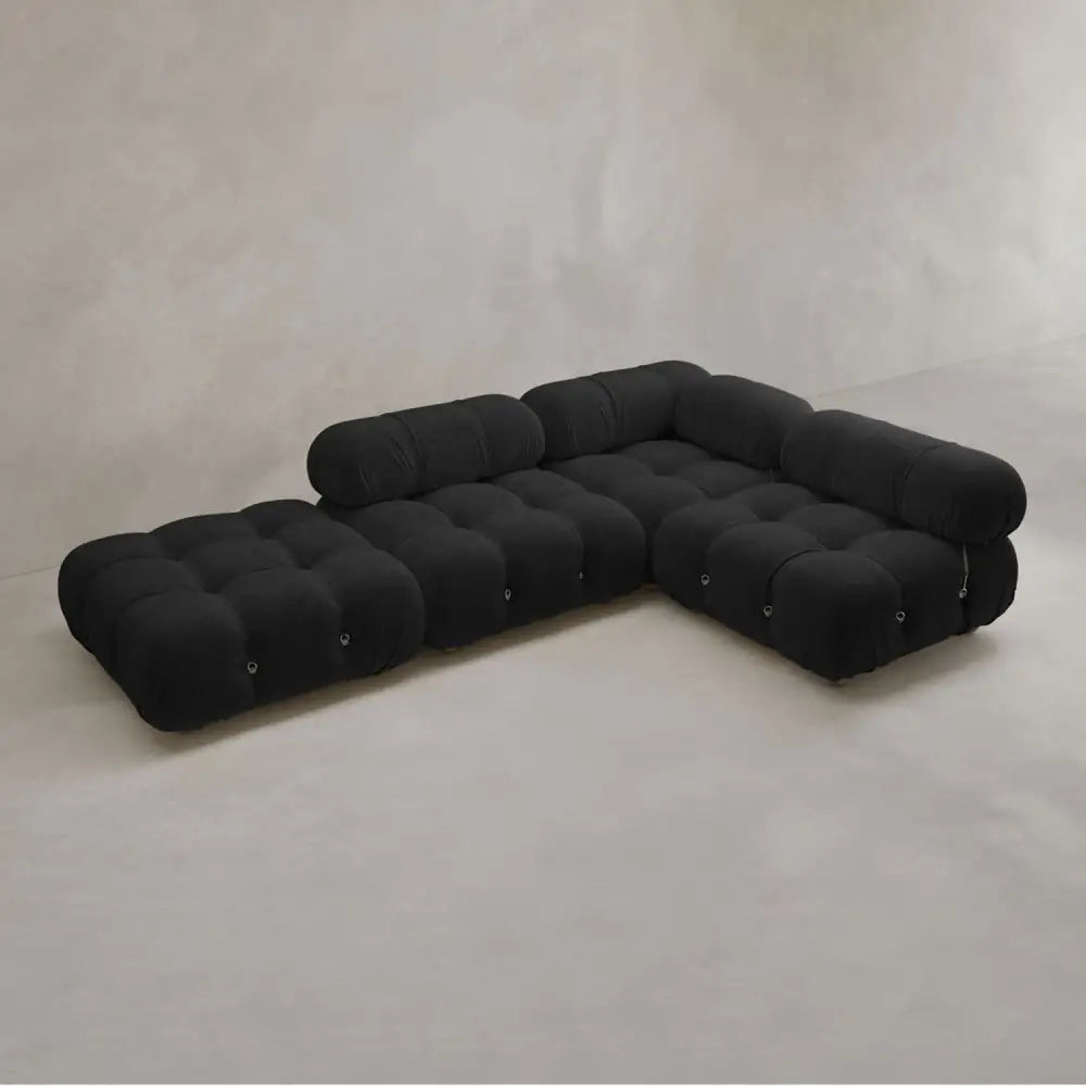The Belmont Sofa Combination C is a modern modular black sofa with marshmallow-like curves, three sections, rounded tufted cushions, and low cylindrical backrests, set against a plain light-colored wall and floor.
