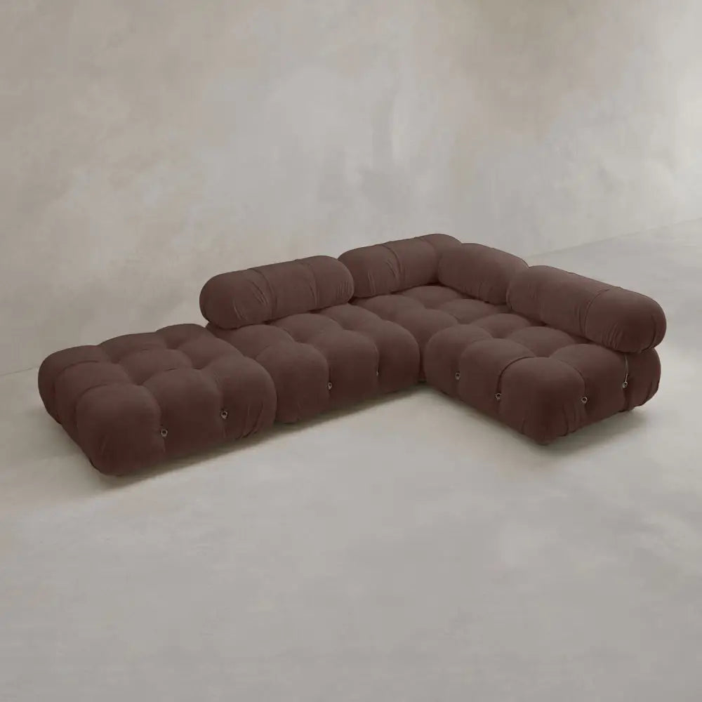 The Belmont Sofa Combination C is a modern, modular brown sectional with tufted cushions and cylindrical headrests, featuring marshmallow-like curves in an L-shape against a light-colored wall and floor.