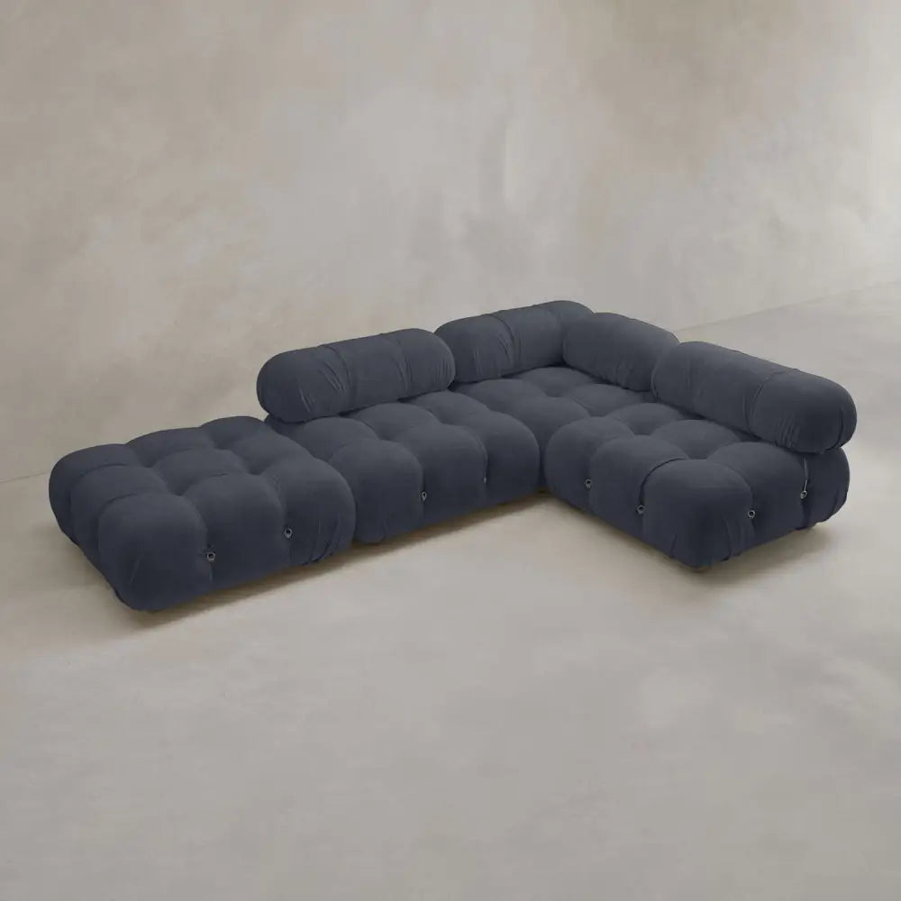 The Belmont Sofa Combination C features dark blue, tufted upholstery and marshmallow-like curves, bringing modern modular style to a minimalist room with light walls and flooring.