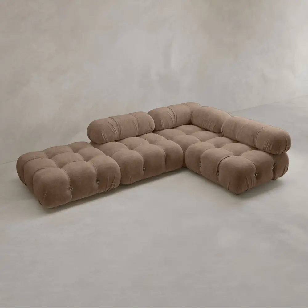 The Belmont Sofa Combination C is a modern, low-profile sectional in soft brown fabric with tufted cushions and marshmallow-like curves, rounded edges, and classic appeal, set against a light gray minimalist background.