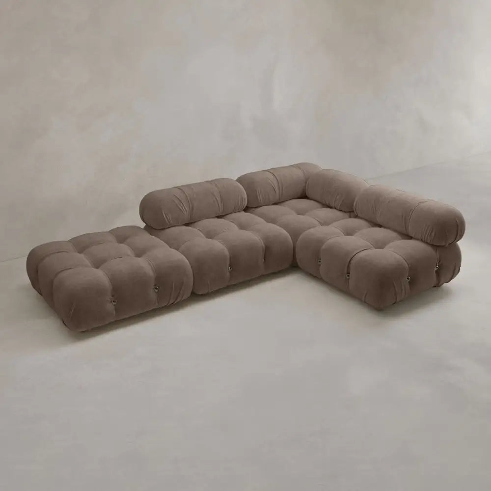 The Belmont Sofa Combination C is a modern, modular brown sectional with tufted cushions and marshmallow-like curves, arranged in an L-shape against a light-colored, minimalistic wall and floor.