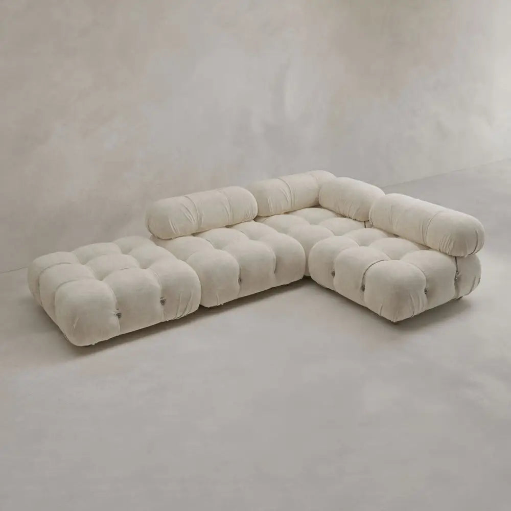 The Belmont Sofa Combination C is a modern, cream-colored modular sectional with tufted, marshmallow-like curves and low, curved backrests, arranged in an L-shape on a light gray minimalist floor and background.