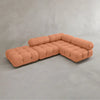 The Belmont Sofa Combination C, a modular tufted sectional with marshmallow-like curves in soft peach, is arranged in an L-shape against a plain light gray concrete wall and floor.