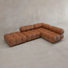The Belmont Sofa Combination C is a modular, L-shaped brown leather sofa with tufted cushions and marshmallow-like curves, positioned on a light-colored floor against a plain beige wall.