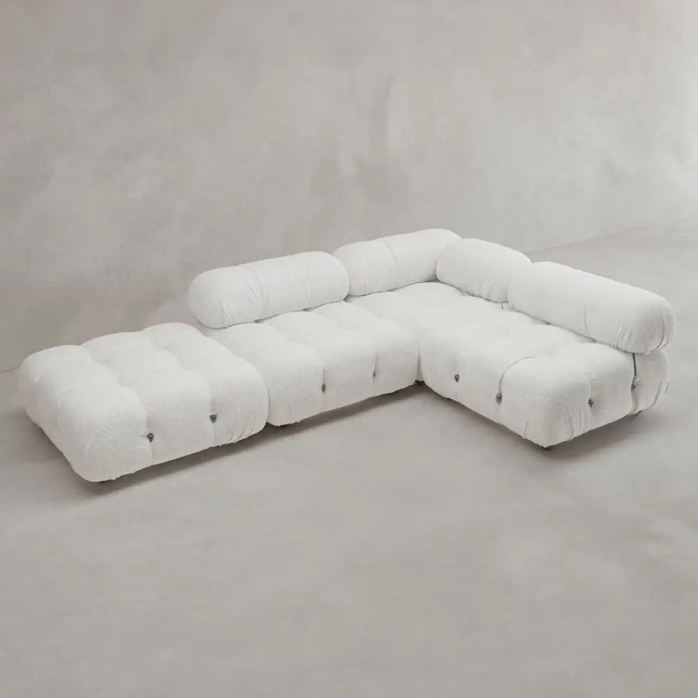 The Belmont Sofa Combination C is a modern, L-shaped modular sofa with marshmallow-like curves, tufted white upholstery, and rounded edges, displayed against a plain light grey wall and floor.
