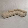 The Belmont Sofa Combination C, a modern light beige modular sectional with marshmallow-like curves and tufted cushions, sits on a smooth light gray floor against a textured off-white wall—an iconic classic of modular design.