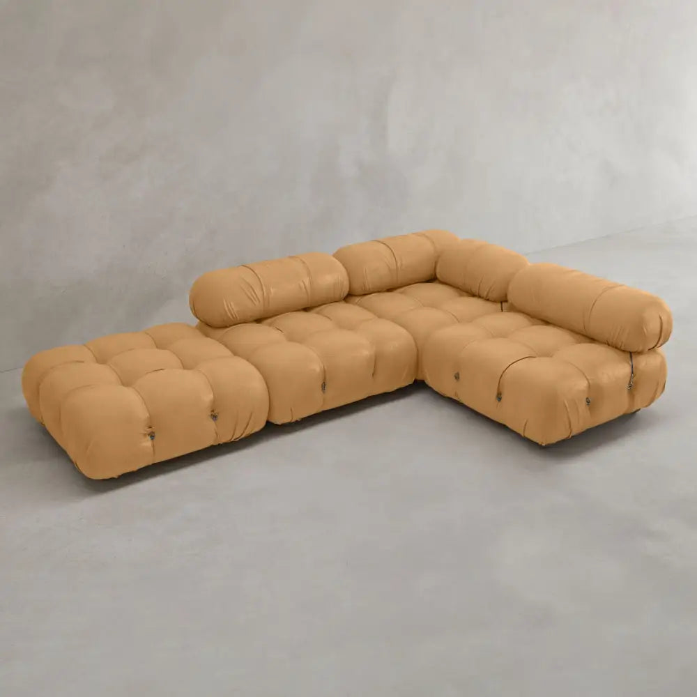 The Belmont Sofa Combination C, a modular tan sectional with tufted, marshmallow-like curves and cylindrical back and arm supports, is arranged in an L-shape against a plain gray wall and floor.