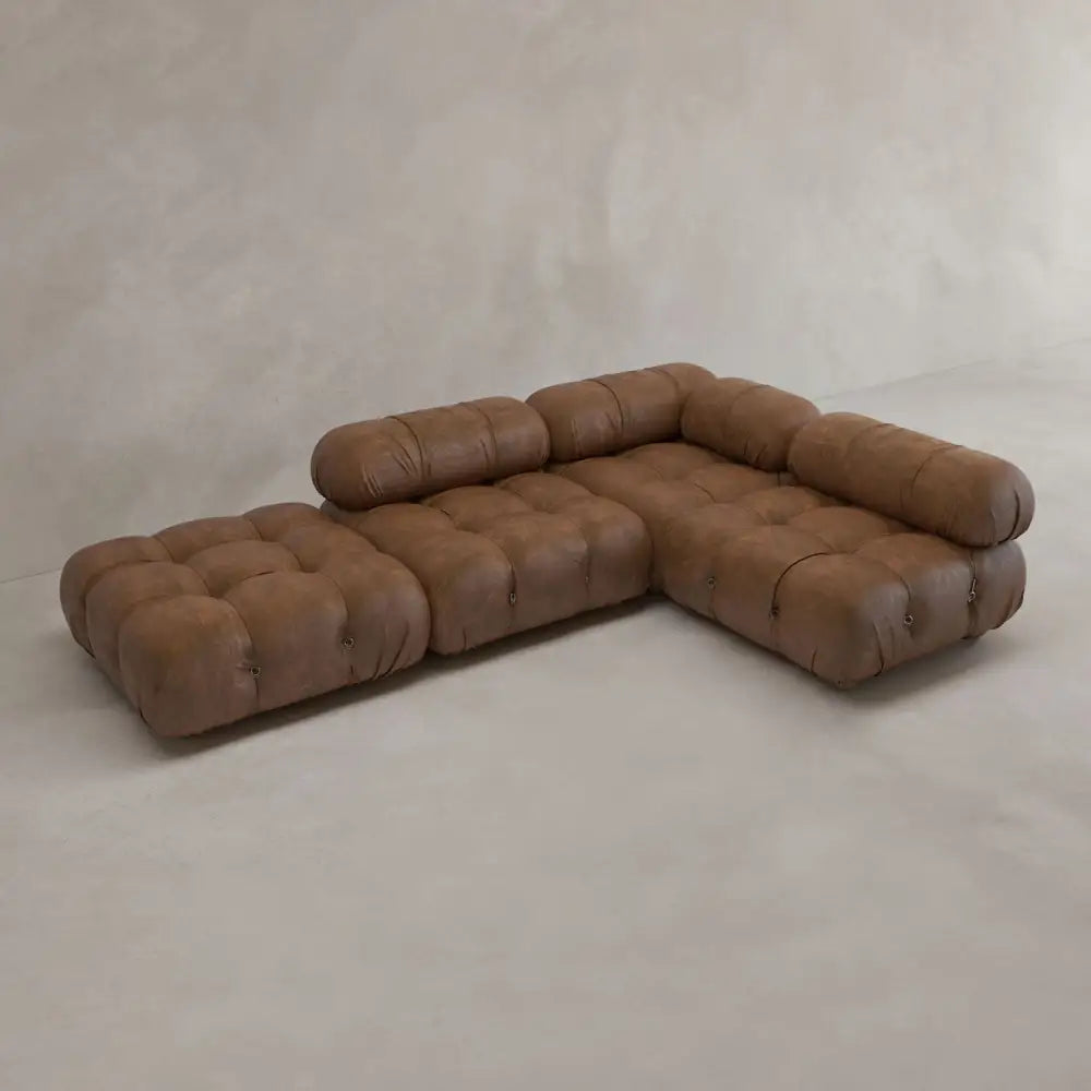 The Belmont Sofa Combination C is a modern, modular brown leather sectional with tufted cushions and marshmallow-like curves, low backrests, set against a plain light beige wall and floor.