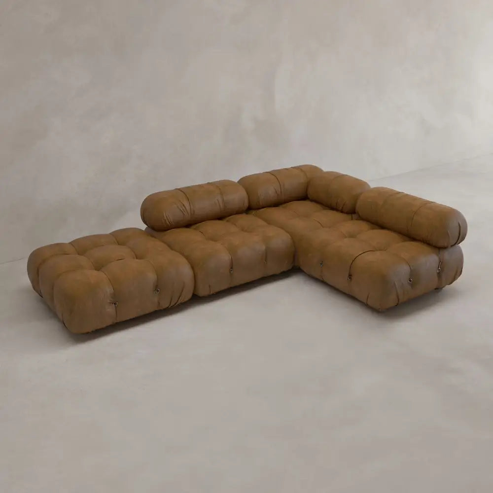 The Belmont Sofa Combination C, a brown tufted modular sectional with marshmallow curves and cylindrical backrests, is arranged in an inviting L-shape on a light floor against a neutral wall.