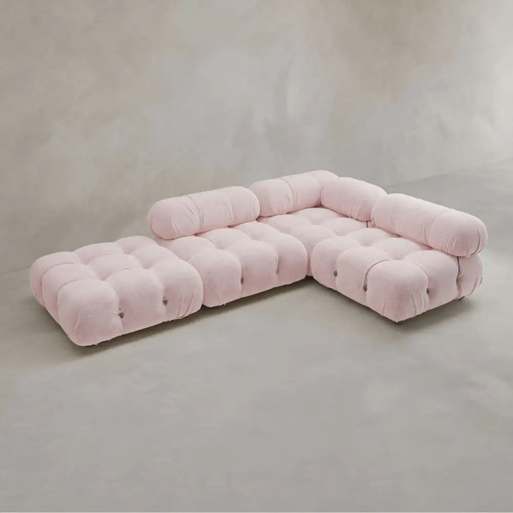 The Belmont Sofa Combination C is a modular, L-shaped pink sofa with tufted cushions and marshmallow-like curves, positioned on a smooth light grey floor against a plain neutral wall.