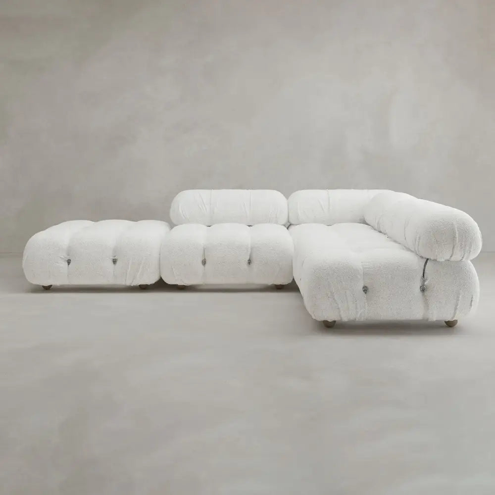 The Belmont Sofa Combination C, a modern modular white sectional with plush tufted curves, is set against a plain light gray wall and floor background.