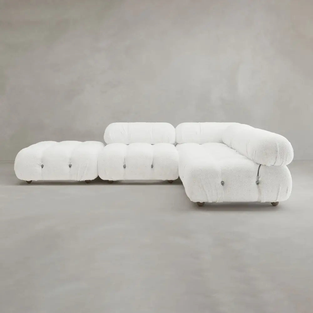 The Belmont Sofa Combination C is a modern white tufted sectional with marshmallow-like curves, rounded edges, and a matching ottoman, featuring a modular design against a plain gray background.