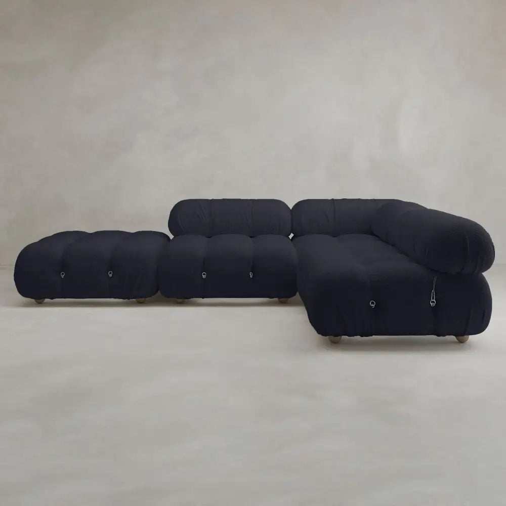 The Belmont Sofa Combination C features a modern, tufted black design with marshmallow-like curves and a low profile, set against a neutral, lightly textured backdrop in a minimalistic room.