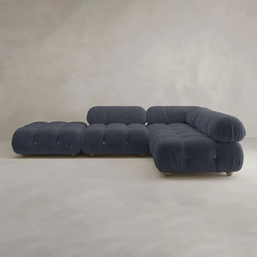 The Belmont Sofa Combination C is a modern, modular navy blue sofa with tufted cushions, marshmallow-like curves, rounded edges, and a matching ottoman, styled against a light gray minimalist background.