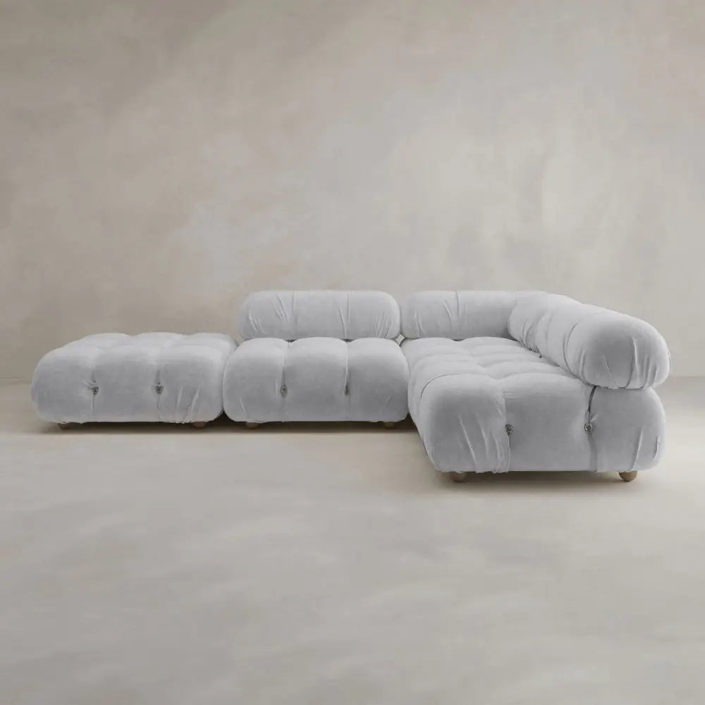 The Belmont Sofa Combination C, with its light gray hue, modern design, plush tufted cushions, and soft curves, sits on a neutral floor against a beige textured wall.