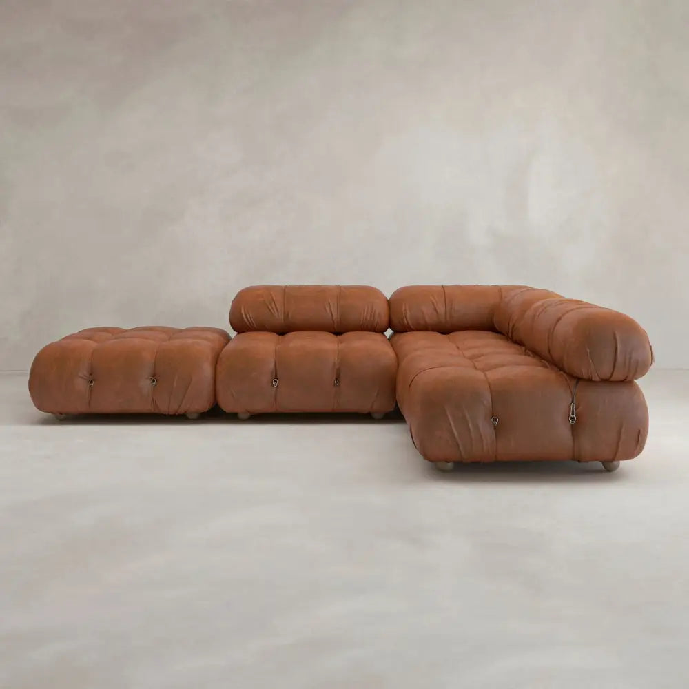 The Belmont Sofa Combination C features brown leather, tufted cushions, and marshmallow-like curves, arranged on a light neutral floor against a textured beige wall—an iconic classic of modular design.