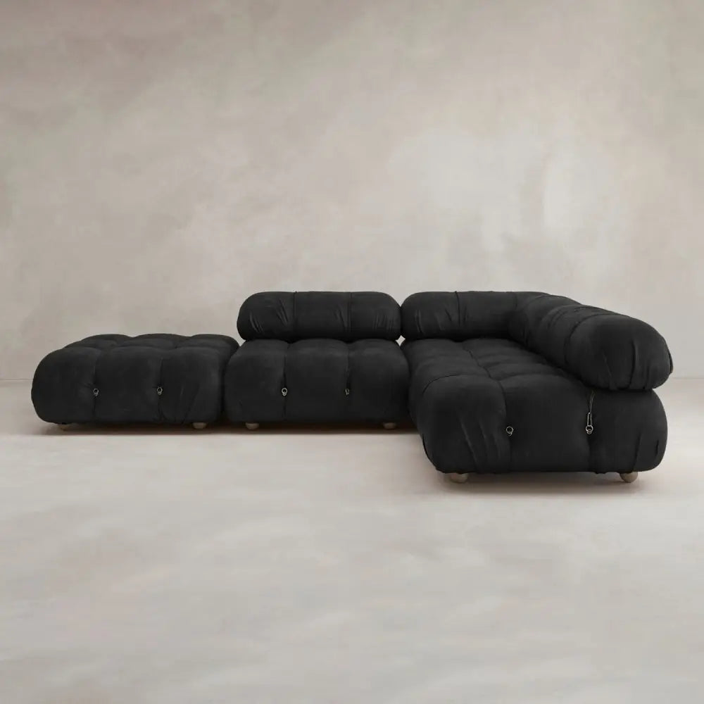 The Belmont Sofa Combination C, featuring a modular design with tufted cushions and black upholstery, is placed on a light floor against a neutral textured wall.