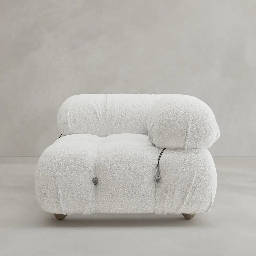 The Belmont Sofa Left Armrest features plush white textured upholstery, marshmallow-like curves, rounded edges, and minimalist metal accents, set against a plain light gray wall and floor.